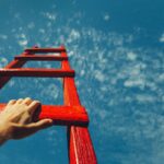 Man's hand reaching for a ladder leading to a blue sky.Development Attainment Motivation Career Growth Concept.